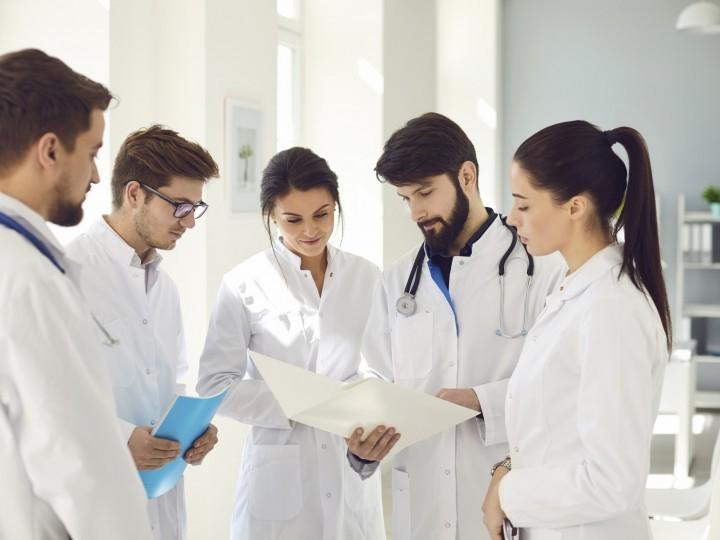 A group of students wearing lab coats gather and observe health chart in hospital setting